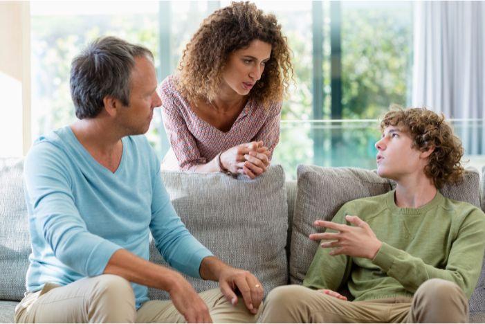 Teenage boy looking upset while his mother places a supportive hand on his shoulder during a difficult family conversation about conflict at home
